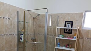 A bathroom with a glass-enclosed shower, a white sink, and a shelf with toiletries. - Room-lady Room in Puntacana (Punta Cana)