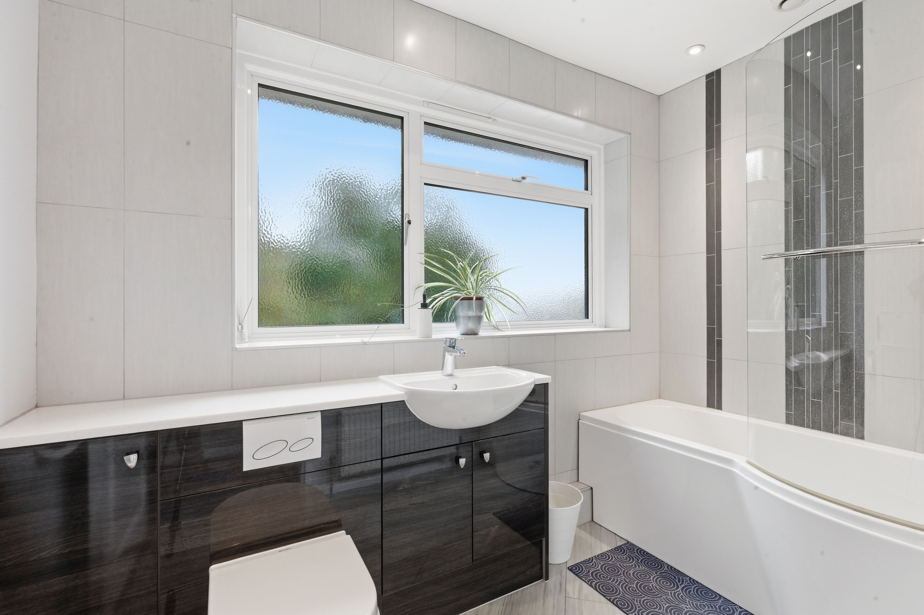 A modern bathroom with a large window, a sink, a bathtub, and a shower area.