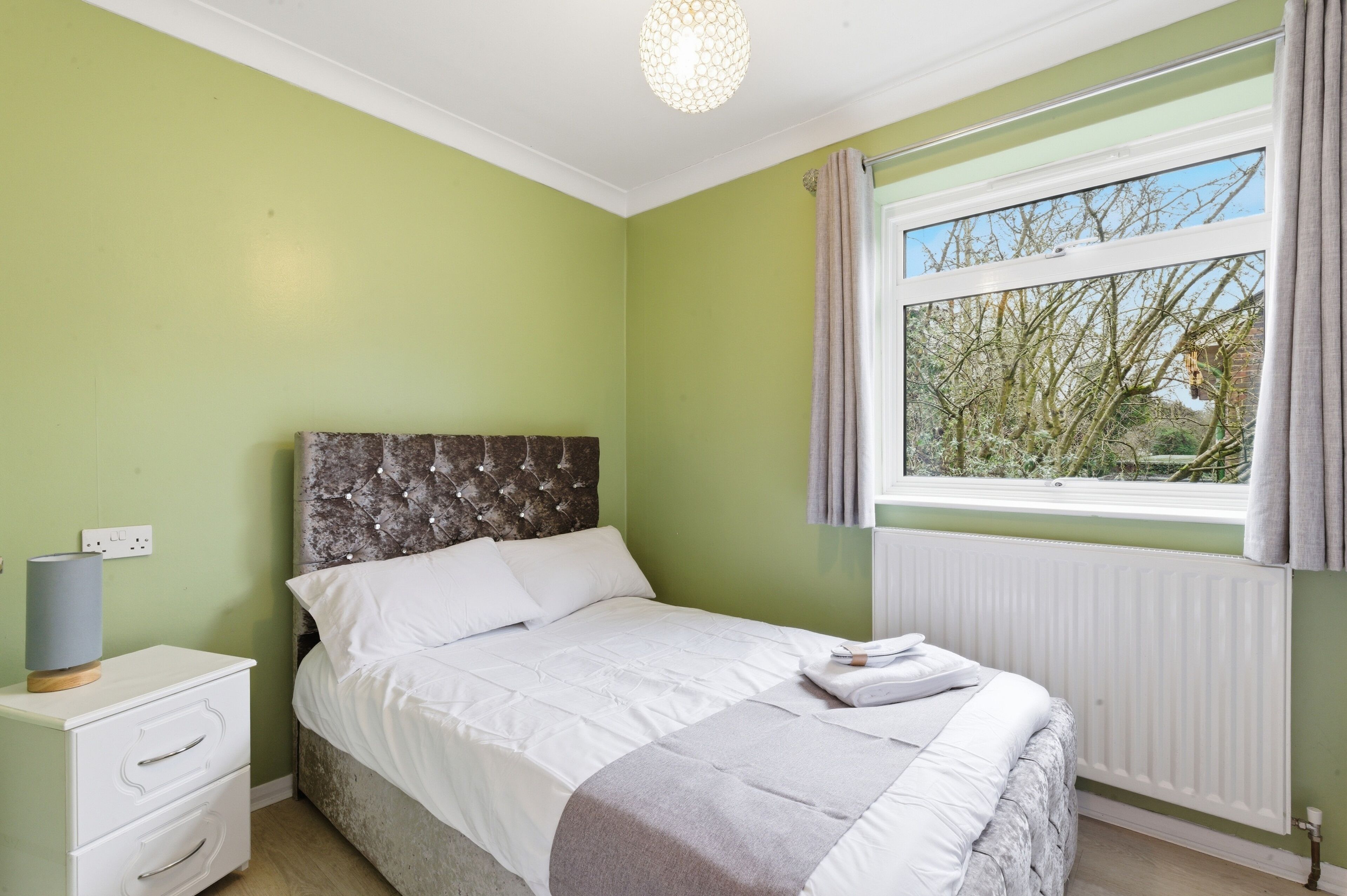 A bedroom with a bed, a nightstand, a lamp, and a window with curtains.