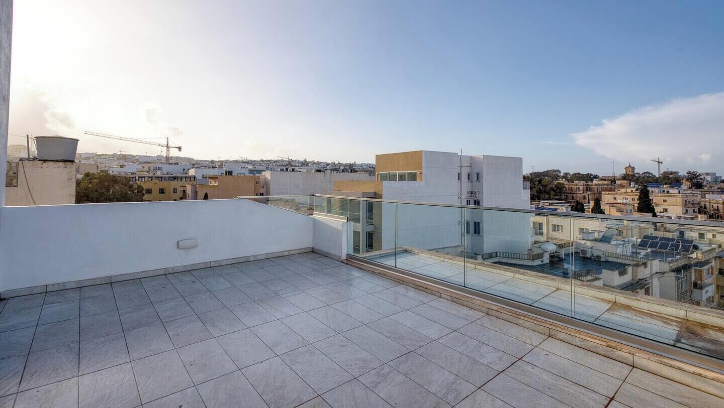A rooftop terrace with a glass balustrade, offering a view of the cityscape.