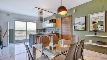 Une cuisine moderne avec une table et des chaises en verre, une vue dégagée grâce à de grandes fenêtres et un panneau indiquant la sortie de secours.