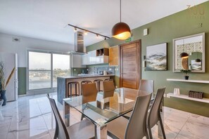 Una cocina moderna con una mesa y sillas de vidrio, vistas a través de amplios ventanales y un letrero de salida de incendios.