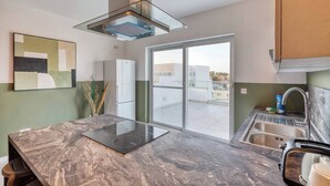 Een moderne keuken met een marmeren aanrecht, een roestvrijstalen afzuigkap, een koelkast, een spoelbak en een schuifdeur naar een balkon.