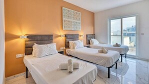 Hotelkamer met drie bedden, elk voorzien van een hoofdbord en bedlampjes. Groot raam met uitzicht op de stad.