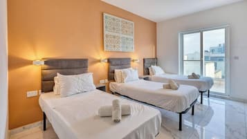 Una camera d'albergo con tre letti, ognuno dotato di testiera e lampade sui comodini. Ampia finestra con vista sulla città.
