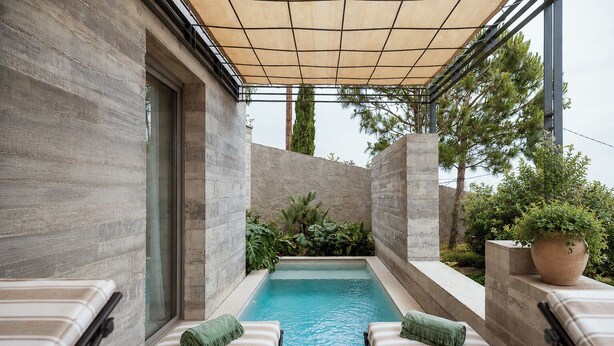 Zwembadgedeelte met betegelde vloer, twee ligstoelen met groene kussens, een pergola met beige zonnedak en een potplant.