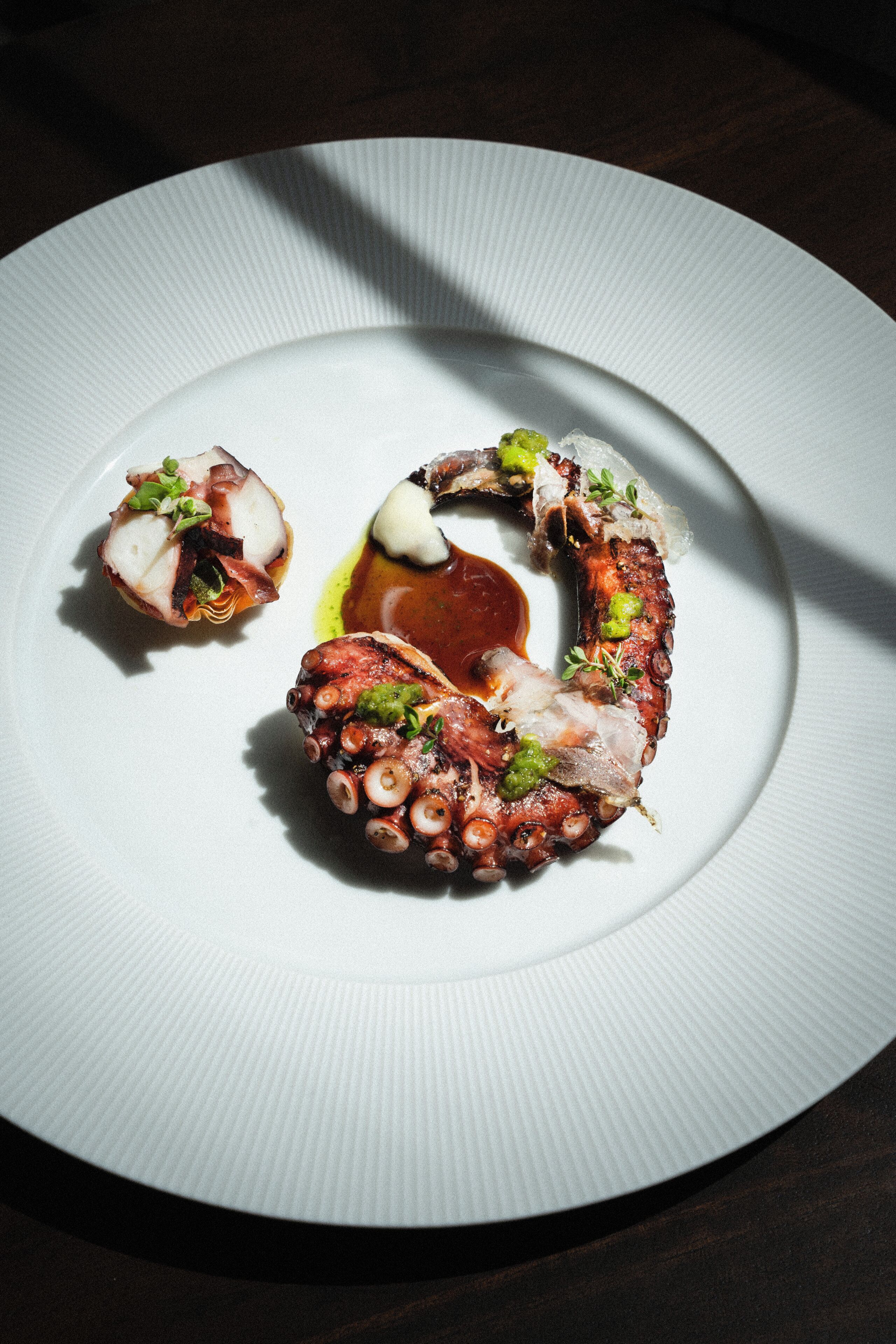 Un plato blanco con pulpo y una pequeña porción de salsa.