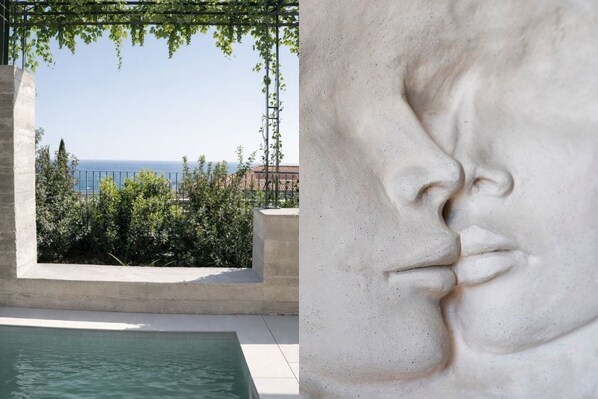Una piscina con vista al mar, una estructura de concreto y un primer plano de una escultura de piedra.