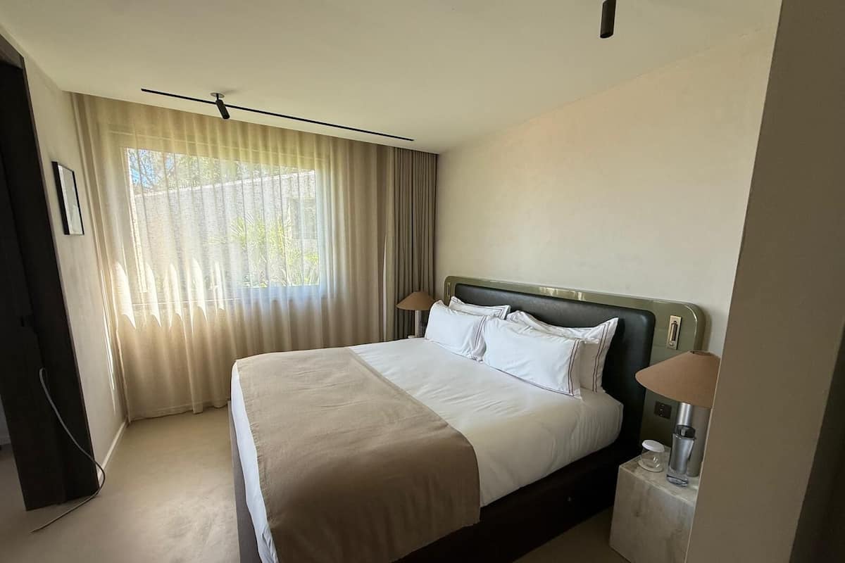 A hotel room with a bed, bedside lamps, a nightstand, and a window with curtains.