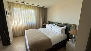 Een hotelkamer met een bed, nachtlampjes, een nachtkastje en een raam met gordijnen.