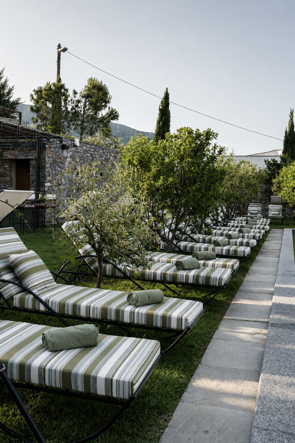 Outdoor lounge chairs with striped cushions, a stone wall, and a pathway.