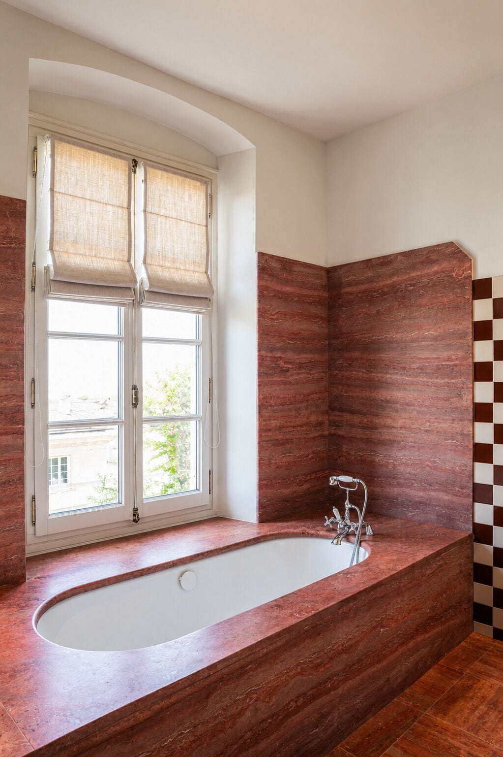 Un bagno con una vasca freestanding, una finestra con persiane e un rivestimento in piastrelle a scacchi.