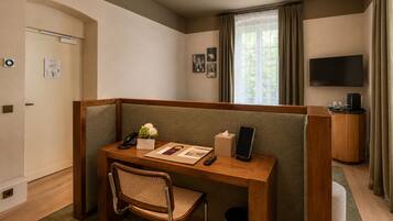 Une chambre d’hôtel avec un bureau en bois, une chaise, un téléphone, une boîte de mouchoirs, une télécommande, une tablette, un téléviseur et une fenêtre avec des rideaux.