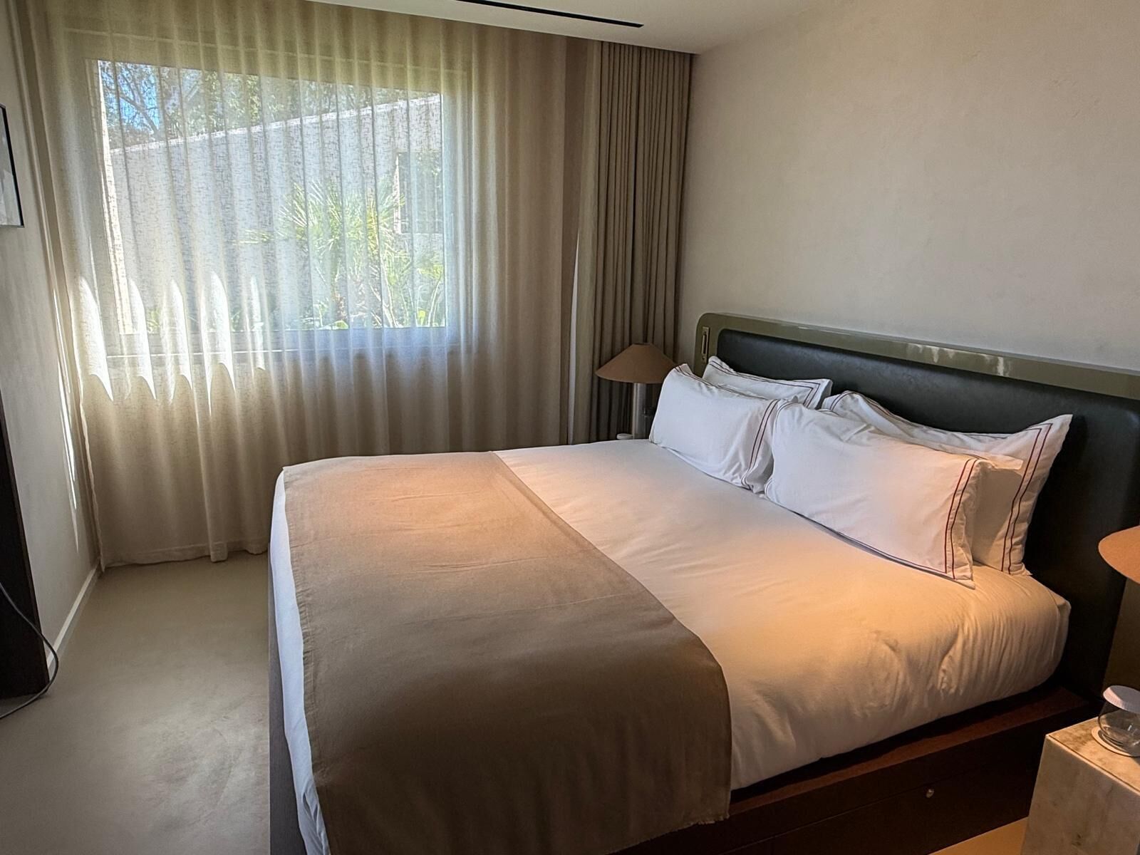 Une chambre d’hôtel avec un lit, des rideaux, une lampe et une fenêtre.