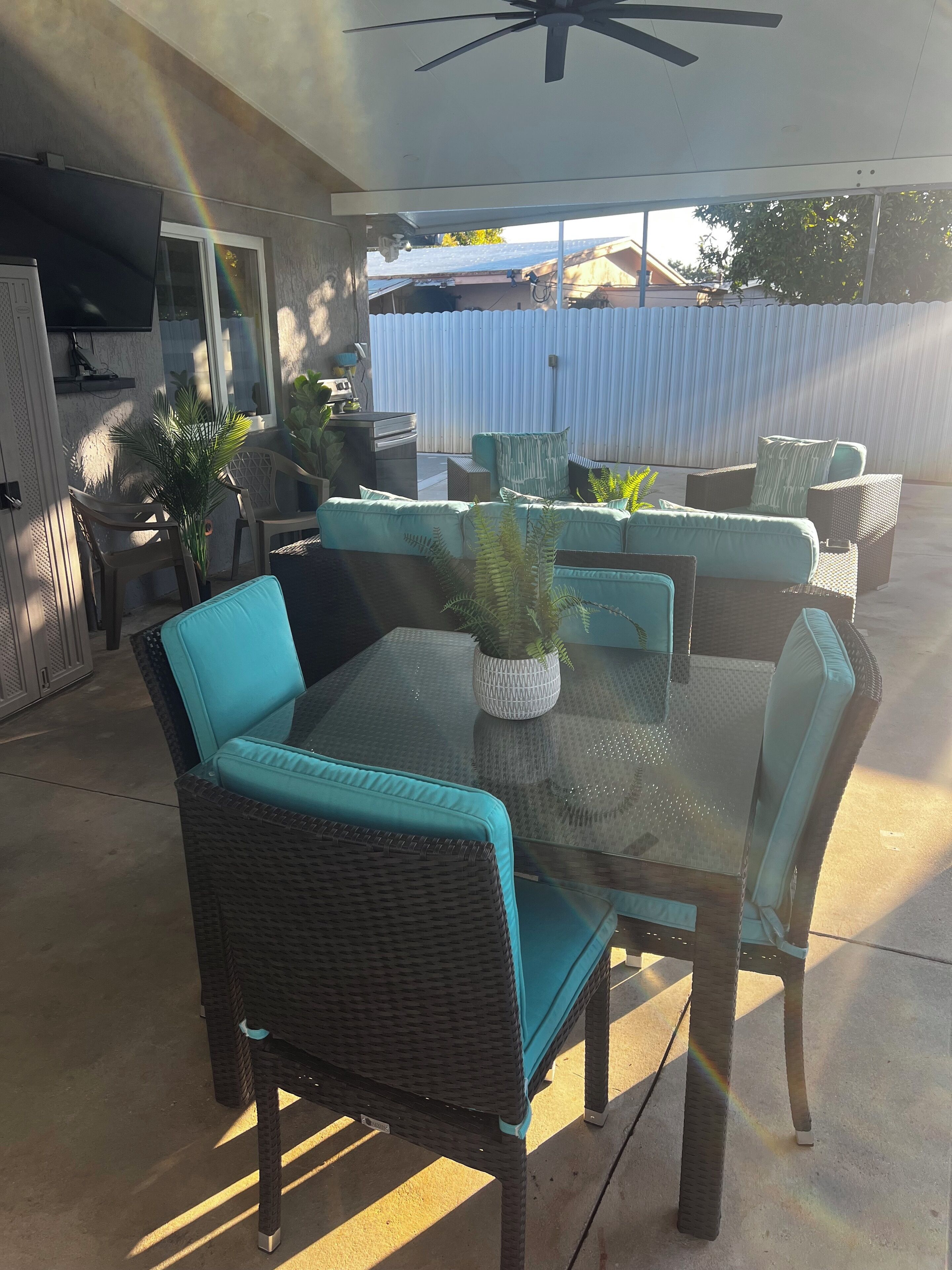 An outdoor patio with wicker furniture, a glass table, and potted plants.