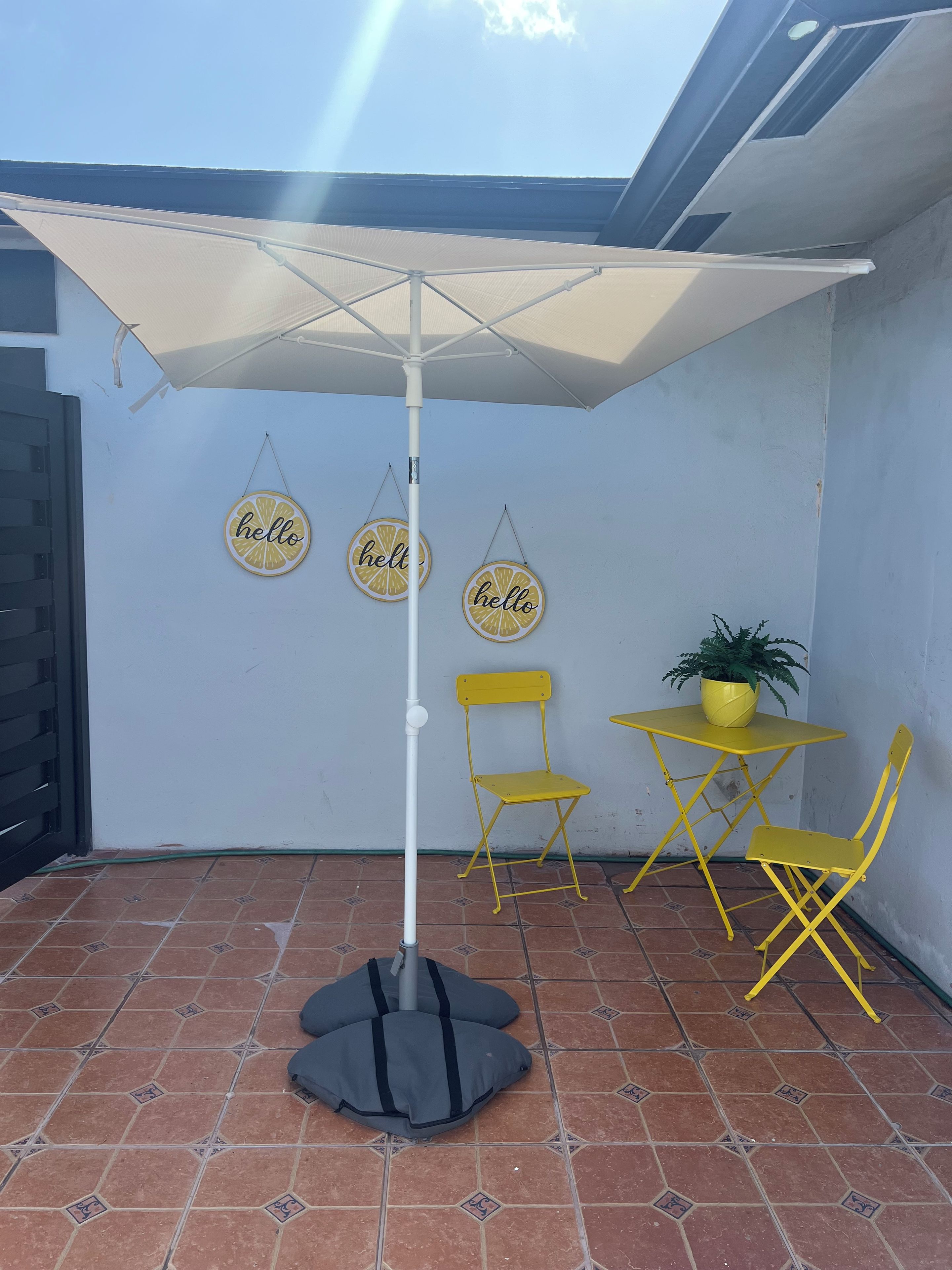A patio area with a white umbrella, yellow chairs, a small table, and a potted plant.