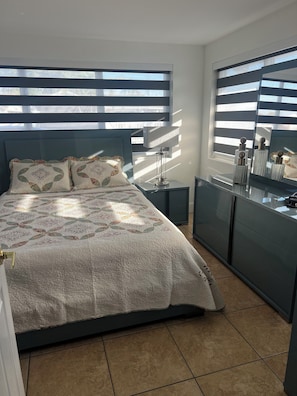 A bedroom with a bed, bedside table, dresser, and a mirror.