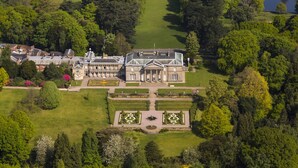 Vue aérienne d’un vaste domaine historique, avec de magnifiques jardins, une pelouse centrale symétrique et une pelouse d’entrée aménagée avec une fontaine.