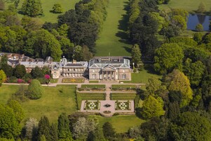 Una vista aerea di una grande tenuta storica con ampi giardini, un prato centrale simmetrico e un giardino formale sul davanti con una fontana.
