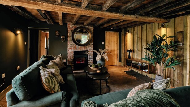 Un intérieur rustique avec des poutres apparentes, une cheminée et un coin salon confortable avec un canapé et des fauteuils.