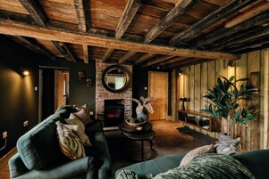 Un interno rustico con travi a vista in legno, un camino e un angolo salotto accogliente con divano e poltrone.