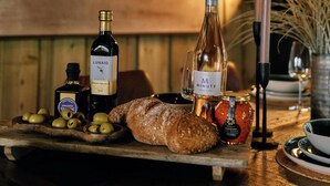 Une table en bois sur laquelle se trouvent une bouteille de vin Lunaio, un pot de miel, des olives, une miche de pain et une bougie.