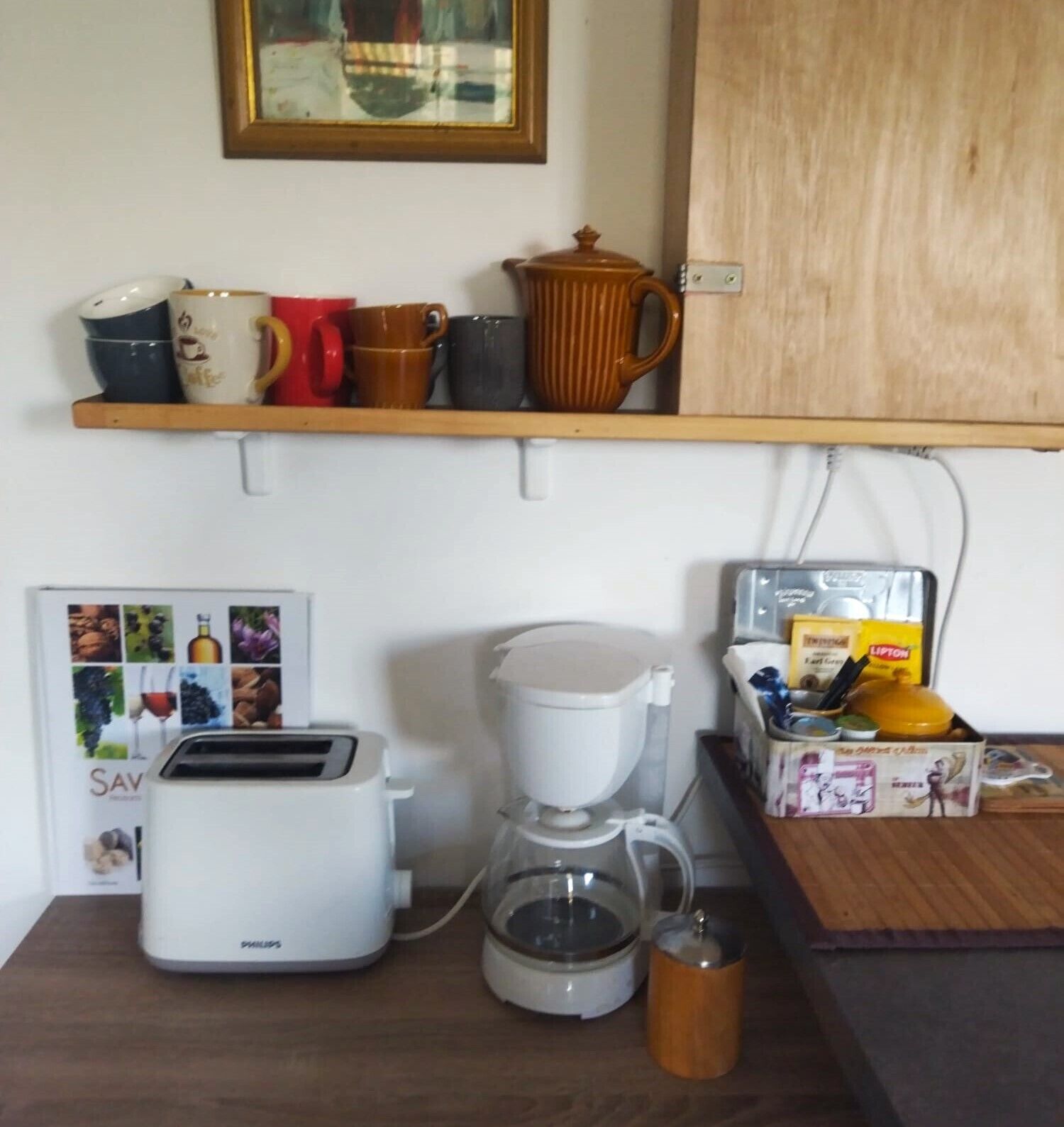 Una cocina con tostadora, cafetera y una repisa con tazas.