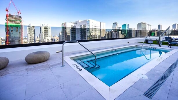 Una piscina en la azotea con vistas al horizonte urbano, incluyendo edificios altos y grúas de construcción.