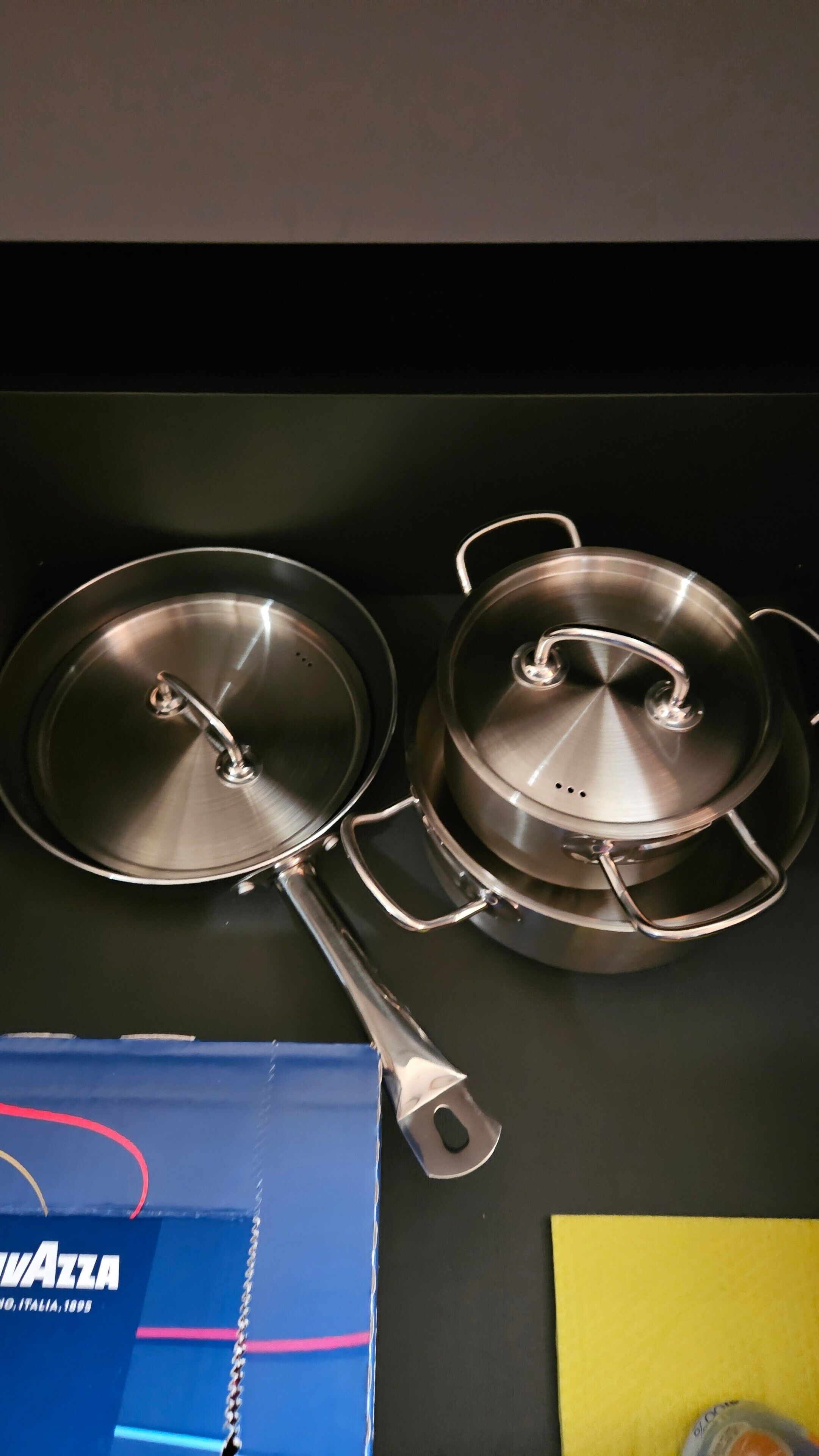 Deux casseroles en acier inoxydable, dotées de couvercles, posées sur une surface noire.
