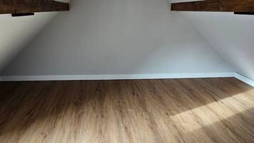 Una stanza mansardata con travi in legno, soffitto spiovente e pavimento in legno.