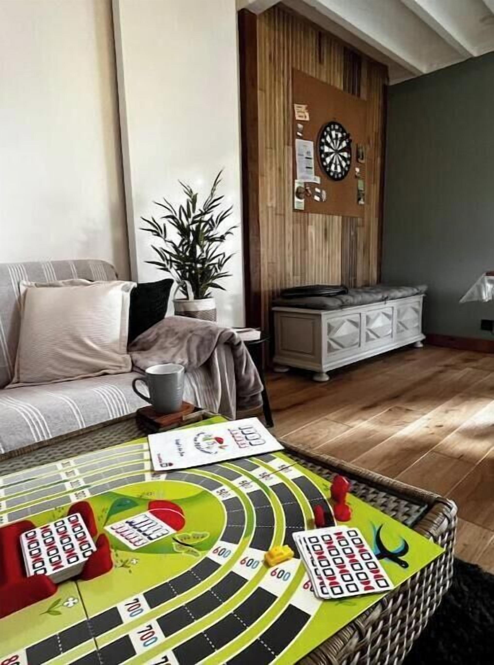 Ein Wohnzimmer mit Dartscheibe, einer Couch, einem Couchtisch mit einem Gesellschaftsspiel und einer Zimmerpflanze.