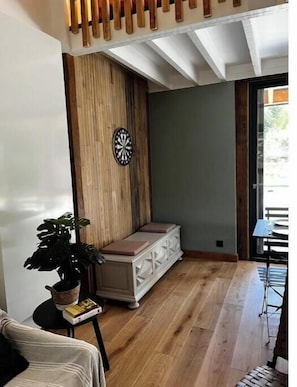 A room with a wooden bench, a dartboard, a potted plant, and a table with chairs. - Bol d'air Normandie (Capelle-les-Grands)