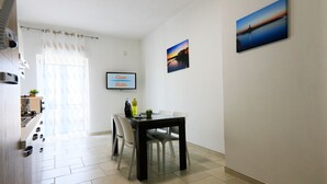 A modern kitchen with a dining area, a TV displaying 'Casa Bella', and a painting of a sunset. - Casa Bella (Vieste)