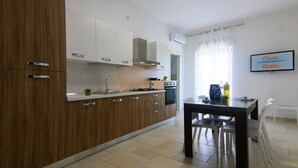 A modern kitchen with wooden cabinets, a gas stove, and a dining area with a table and chairs. - Casa Bella (Vieste)