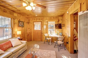 Interior acogedor de una cabaña con techo de madera, un sofá con un cojín que dice 'blessed', una mesa de comedor con sillas y una ventana pequeña con vistas.