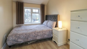 A bedroom with a bed, a nightstand, a dresser, and a window with curtains. - Headmasters Hollow (Watford)