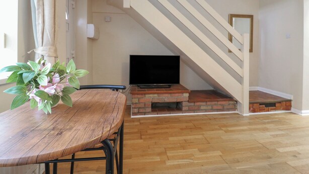 A living room with a wooden table, a brick fireplace, a flat-screen TV, and a staircase with white railings. - Headmasters Hollow (Watford)