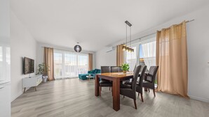 A modern living room with a dining area, large windows, and a flat-screen TV.