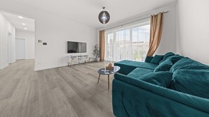 A modern living room with a teal sofa, a flat-screen TV, and a wooden floor.