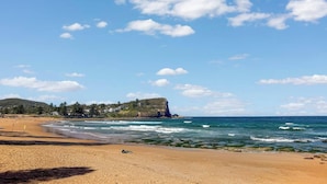 Ein Strand mit einem Felsen im Hintergrund, klarem Himmel und brechenden Wellen.