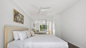 Ein modernes Schlafzimmer mit einem großen Bett, einem Deckenventilator und Blick ins Freie.