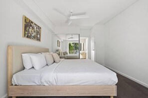 A modern bedroom with a large bed, a ceiling fan, and a view of the outdoors. - Peninsula Sky Walk to Beach Cafs and Golf (Avalon Beach)