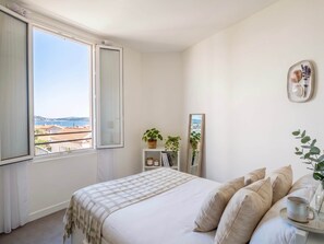 Ein Schlafzimmer mit einem Bett, einem Nachttisch mit einer Tasse, einem Spiegel und Blick aufs Meer.