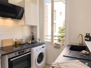 Eine kompakte Küche mit Waschmaschine, Backofen und großem Fenster mit Blick nach außen.