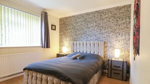 A bedroom with a stone wall, a large bed with a tufted headboard, bedside tables with lamps, and a radiator. - Wizard's Hideaway (Watford)