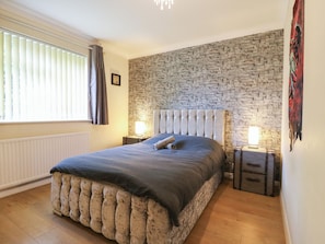 Une chambre avec un mur en pierre, un grand lit doté d’une tête de lit capitonnée, des tables de chevet avec des lampes et un radiateur.