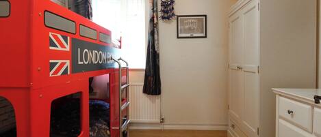 A room with a red double-decker bunk bed labeled "LONDON BUSES," a white dresser, a dreamcatcher, and a framed picture on the wall.