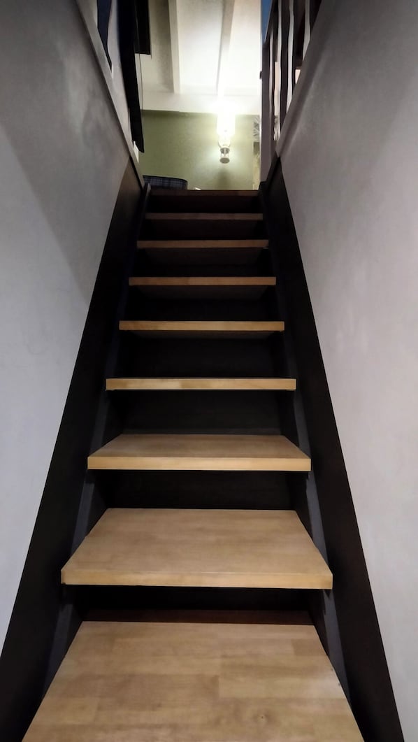 A staircase with wooden steps and black railings, leading to a room with a light fixture on the wall.