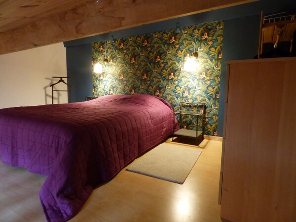 A bedroom with a bed, a nightstand, a dresser, and a wall with a floral pattern. - A vacation rental for 2 people located in the heart of Saillans—charming and peaceful. (Saillans)