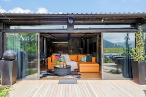 Un interior moderno con sofá y mesa de centro, ventanas amplias y una terraza de madera.